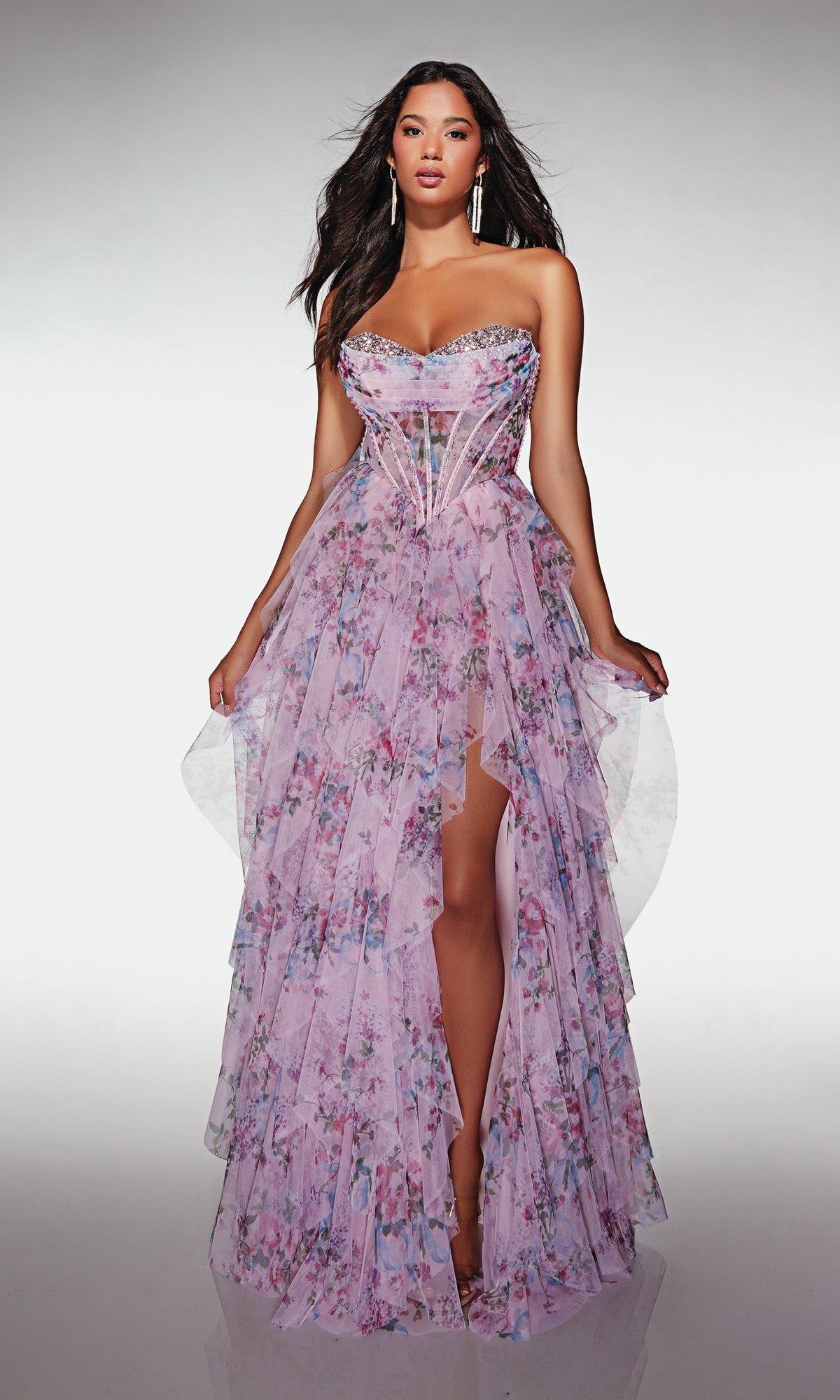 Woman modeling the Alyce 62041 long prom dress in pink/multi, featuring a strapless corset bodice, layered floral print skirt, and high slit, standing against a neutral gradient background.